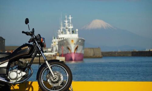 港に停めた黒いバイクSR125の前輪を大きく入れ、その奥に漁船、さらに遠景に雪をかぶった富士山を配置した写真。黄色い車止めのラインが手前を横切り、バイクと富士山と船を一枚に収めようと位置取りに苦戦した一枚。