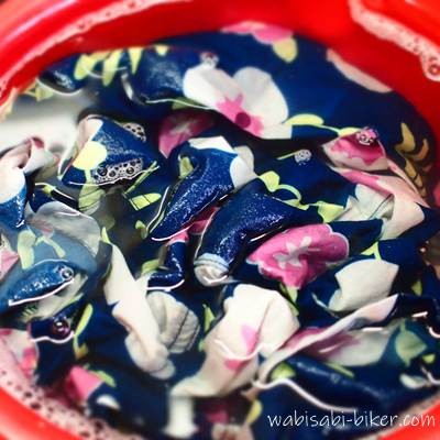 赤いバケツで花柄アロハをつけ置き。泡は少なく、色落ちして青がやや薄まっている様子
