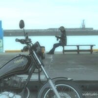 夏の漁港の荷捌き場。手前には黒いバイク(YAMAHA SR125)、奥のベンチにヘルメット姿のライダーが座り、静かな海を前に休憩している。お盆休みで人影はなく、淡い光が港内に満ちている