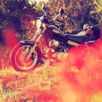 前景に赤くぼけた彼岸花を配し、その奥に黒いバイク(YAMAHA SR125)が停められている。秋の夕陽に照らされ、彼岸花の季節を感じさせる風景。