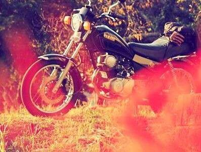 前景に赤くぼけた彼岸花を配し、その奥に黒いバイク(YAMAHA SR125)が停められている。秋の夕陽に照らされ、彼岸花の季節を感じさせる風景。