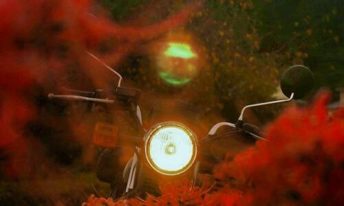 真正面に黒いバイク(YAMAHA SR125)が佇み、ヘッドライトが白く輝いている。ライトの真上には柔らかなフレアが現れ、月に見立てられたような印象を与える。手前には赤くぼけたヒガンバナが広がり、秋の夕暮れ後の風景に溶け込んでいる。