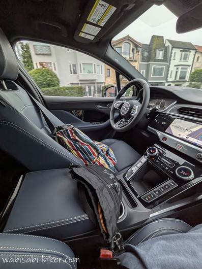 ロボタクシーの車内を助手席側から見た風景。無人運転中のため運転席には誰もおらず、中央のコンソールやモニター、ナビ画面が見える。車内にはカラフルなバッグと黒いポーチが置かれており、窓の外にはサンフランシスコの住宅街が流れている。