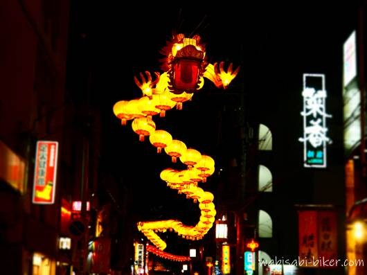 夜の横浜中華街に掲げられた春節燈花の五十節龍。通りの上空に連なる龍のランタン装飾と周囲の建物や看板が写る街景。