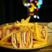 ローズホテル横浜の客室で提供されたルームサービスのクラブハウスサンドとフライドポテトのプレート。背後の窓の外には、ぼかされた中華街の夜景の光が見える。