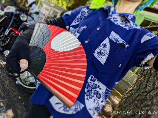 紺色の扇子柄の浴衣リメイクシャツを着て、赤黒の扇子を手にした夏のバイク服装