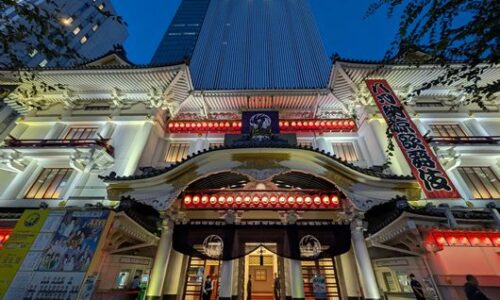 夕暮れの青い空の下でライトアップされた歌舞伎座。正面入口の赤い提灯と看板が写っている。