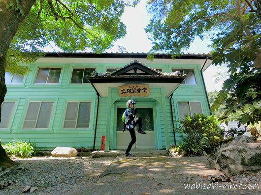 青い浴衣リメイクシャツとヘルメット姿で、木陰の二俣公会堂前に立つセルフスナップ。