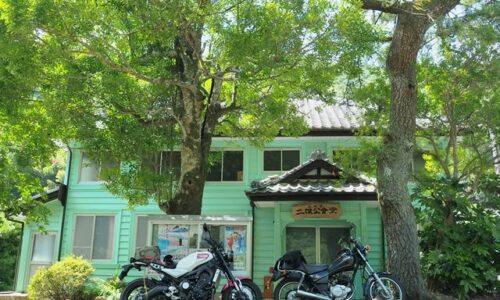 木陰に停めた2台のバイクと旧伊久美銀行として明治期に建てられた二俣公会堂。白いXSR900と黒いSR125が並んでいる。