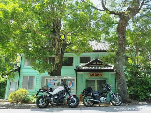 木陰に停めた2台のバイクと旧伊久美銀行として明治期に建てられた二俣公会堂。白いXSR900と黒いSR125が並んでいる。