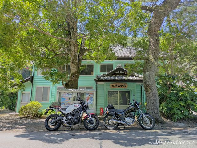 木陰に停めた2台のバイクと旧伊久美銀行として明治期に建てられた二俣公会堂。白いXSR900と黒いSR125が並んでいる。