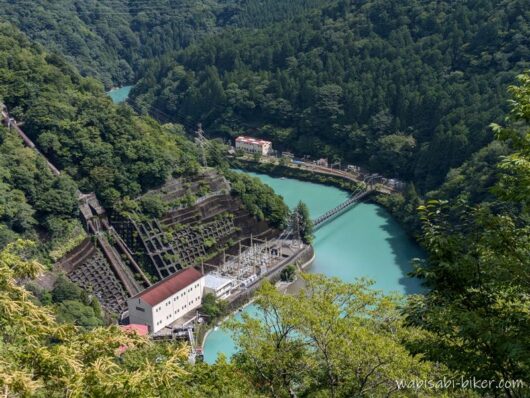 県道から見下ろした奥泉発電所と井川線のアプトいちしろ駅。緑の山々に囲まれた大井川に吊り橋がかかる風景。