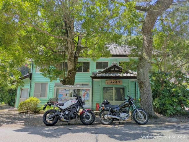木陰に停めた2台のバイクと旧伊久美銀行として明治期に建てられた二俣公会堂。白いXSR900と黒いSR125が並んでいる。