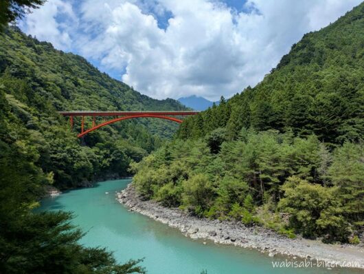 井川線の車窓から眺めた、大井川に架かる赤い泉大橋と緑の山々。