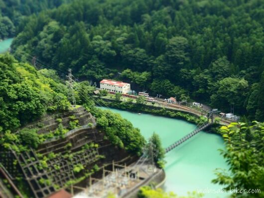 県道から見下ろしたアプトいちしろ駅に停車する井川線の列車。大井川と吊り橋、周囲の山々を望む風景。