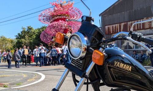 御前崎市の秋祭りで、華やかな祭り屋台と人々を背景に停めた黒いバイクSR125。
