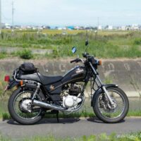 川沿いの道に停めた黒いヤマハSR125。田園風景を背景にしたバイクのサイドビュー。