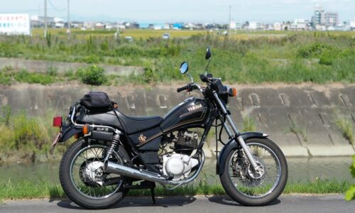 川沿いの道に停めた黒いヤマハSR125。田園風景を背景にしたバイクのサイドビュー。