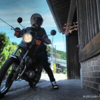 日坂宿の藤文脇に停めた黒いバイクSR125と、ヘルメット姿の乗り手のセルフスナップ。軒先には祭りの花飾りが見える。