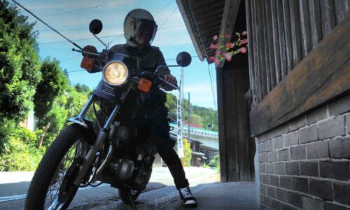 日坂宿の藤文脇に停めた黒いバイクSR125と、ヘルメット姿の乗り手のセルフスナップ。軒先には祭りの花飾りが見える。